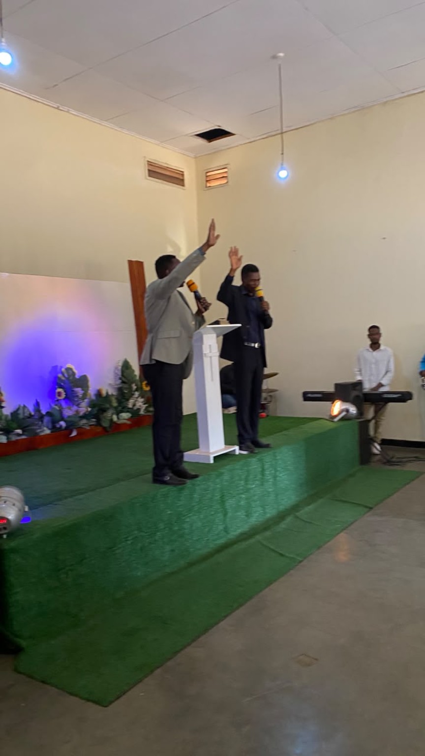 Two ministry leaders holding microphones with hands raised at the front of the church.