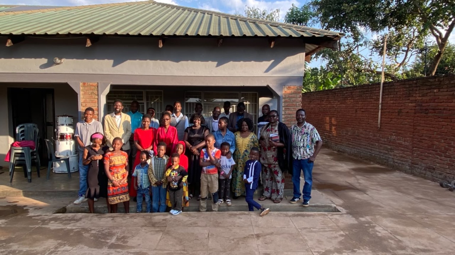 Church family members posing together outside a building with a veranda.