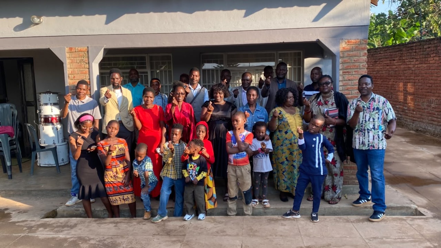 Adults and children standing together for a group photograph outside.