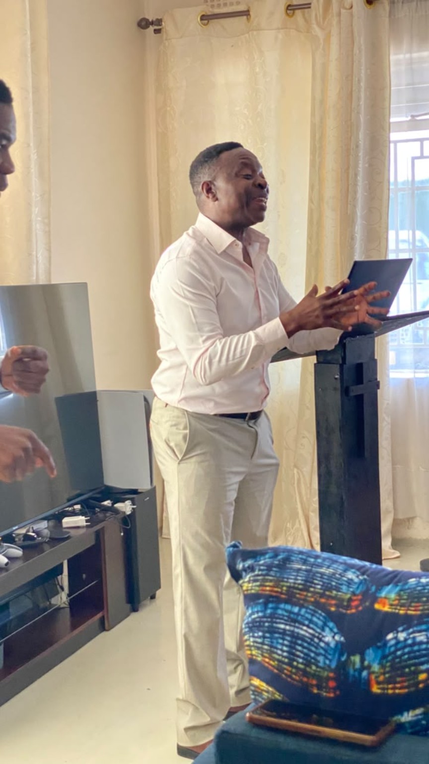 A speaker in a white shirt gesturing beside a lectern and laptop.