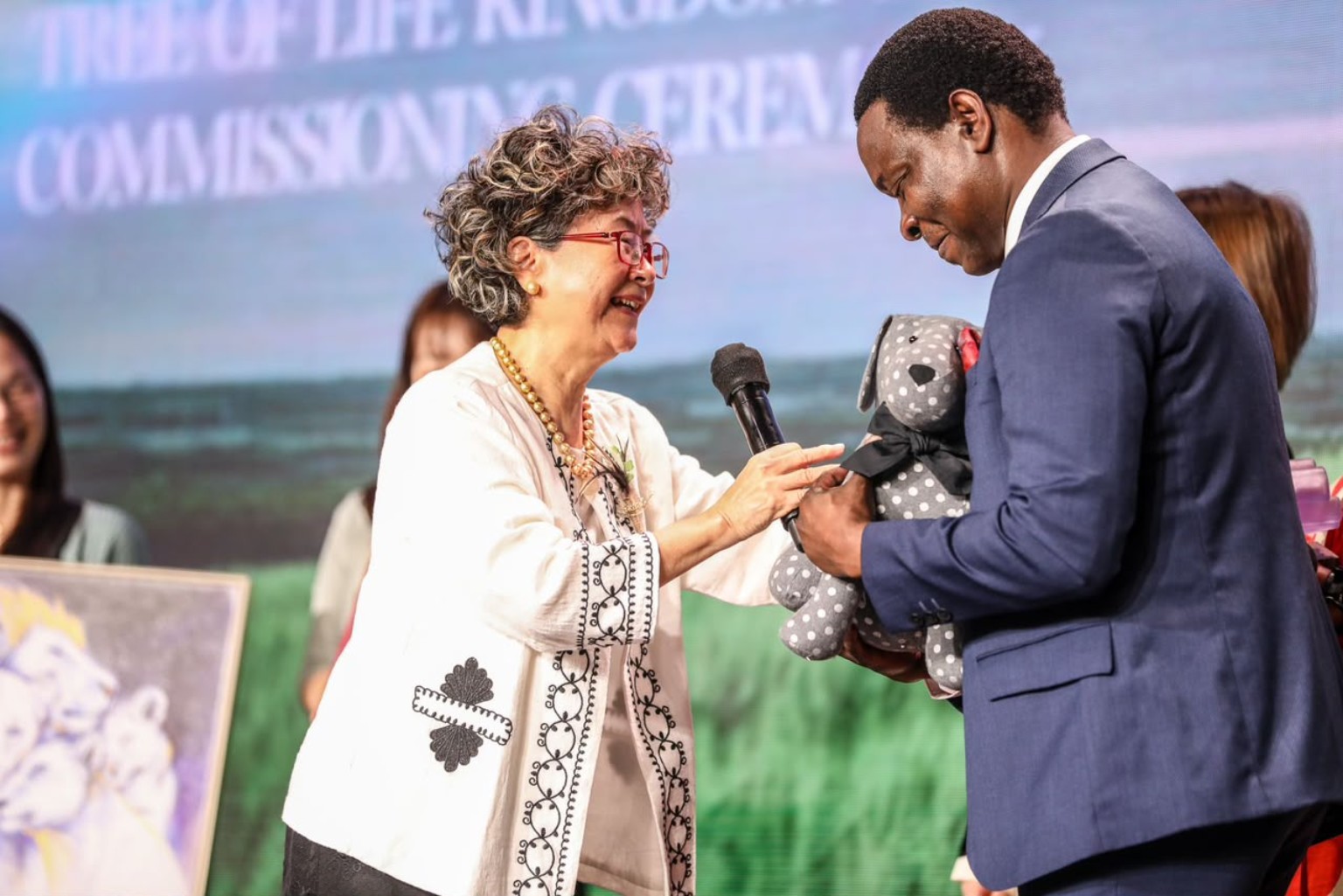 A woman presenting a wrapped gift to a man on the commissioning stage.