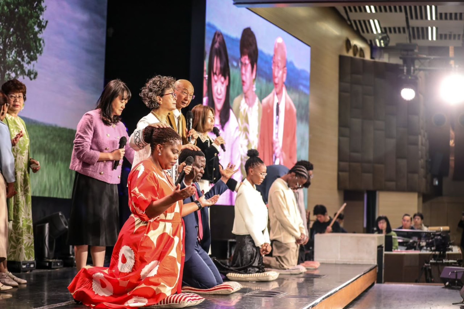 Family members kneeling on stage as ministry leaders pray with them.