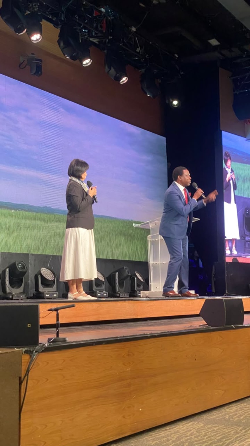 A speaker addressing the congregation alongside another speaker on a large stage.