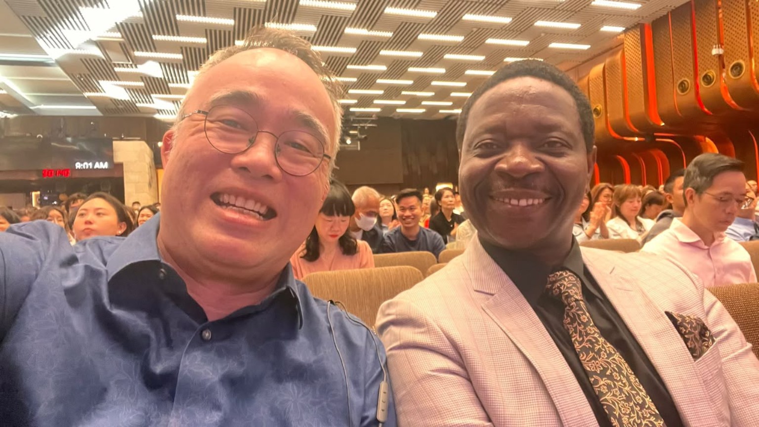 Two smiling men taking a photograph together in a church auditorium.