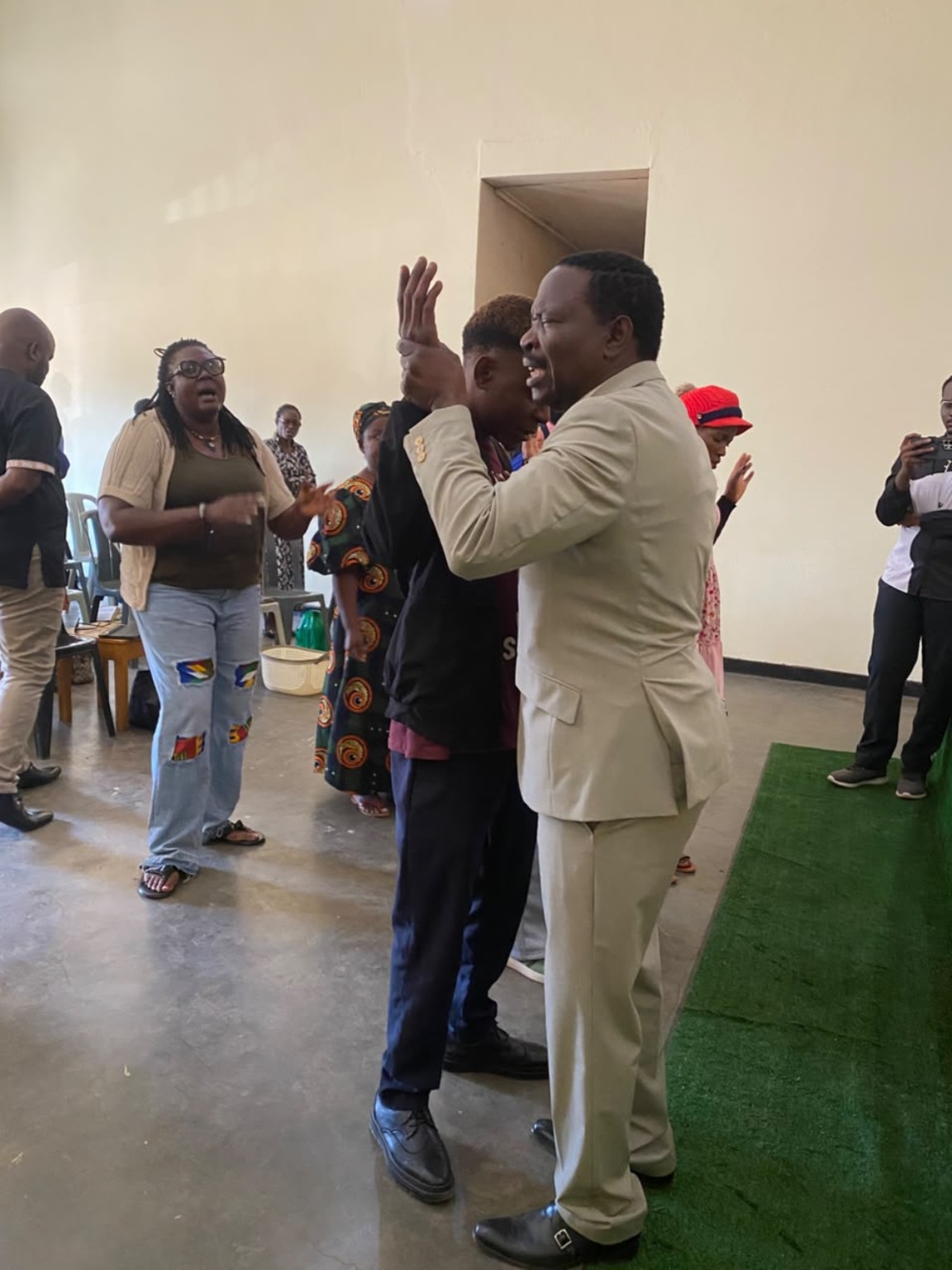 A ministry leader in a cream suit praying with a church member beside the green platform.